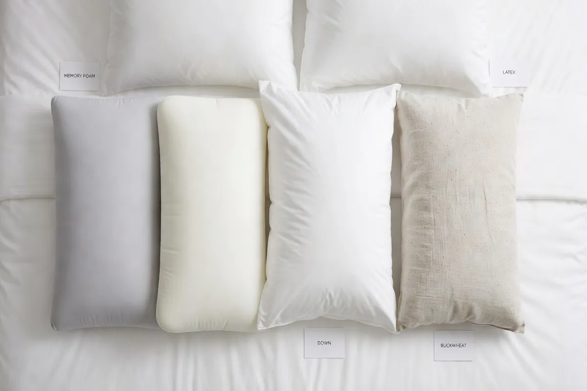 Différents types d'oreillers sur lit blanc : mousse viscoélastique, latex, plumes, sarrasin